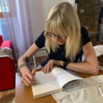 a scrittrice Giovanna Ceriotti mentre scrive una dedica personalizzata su un libro, seduta al tavolo all'interno del B&B La Dimora di Tommaso